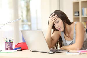 Frustrated woman at her desk, holding her head and looking at a laptop
